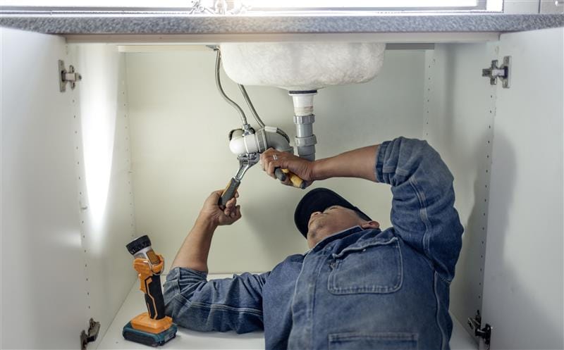 Plumber repairing pipes beneath a bathroom sink in Newark